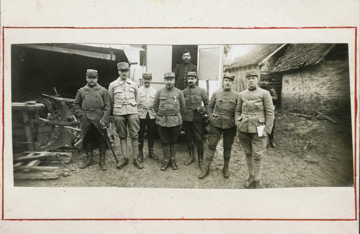Groupe de neuf militaires dans une cour de ferme devant l'auto-laboratoire photographique : photographie noir et blanc.