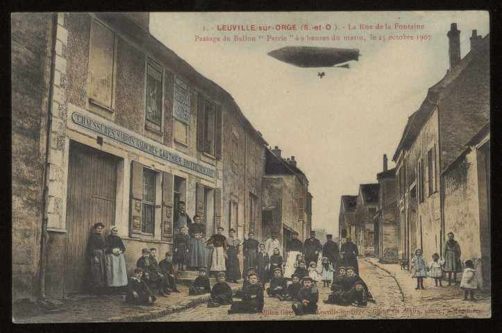 LEUVILLE-SUR-ORGE. - La rue de la fontaine. Passage du ballon dirigeable "Patrie" à 9h du matin le 15 octobre 1907. Edition Gauthier, Leuville-sur-Orge, cliché Ch. Maire, Montlhéry, colorisée. 