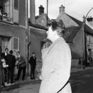 Jean MARAIS marche dans la rue nouvellement rebaptisée et parle avec les habitants de la commune de MILLY-LA-FORET, 22 mars 1964, 1 négatif noir et blanc, 1 photographie noir et blanc, 1964.