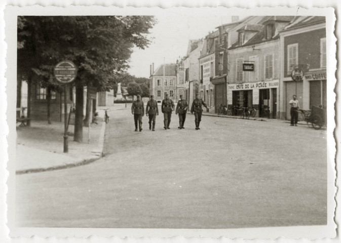 DRAVEIL.- Occupation de la ville par l'armée allemande : des soldats allemands marchant dans une rue bordant la place de la République, près de l'église, avec au fond, l'ancien emplacement du monument aux morts et l'ancienne mairie, N et B. Dim. 6 x 8 cm. 
